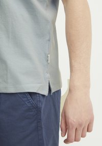 Lyseblå bomulls t-skjorte med sidesplitter, flate sømmer og et lite merke ved kanten. Kombinert med marineblå shorts, som gir en avslappet passform.