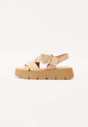 Beige sandaal met open teen, brede gekruiste banden, gouden gesp, elastisch achterbandje en dikke profielzool in lichtbruin.
