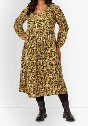 Woman wearing a long-sleeve black midi dress with small yellow flowers, black leggings, black boots, and layered silver necklaces.
