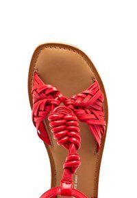 Sandale rouge tressée avec des sangles entrelacées et un accent circulaire. La semelle est en cuir lisse couleur tan, avec un design plat.