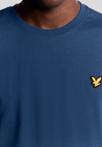 T-shirt in cotone blu navy con scollatura rotonda, caratterizzata da un logo di un aquila ricamato in giallo sul lato sinistro del petto.