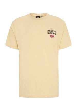 Beige T-shirt met korte mouwen en zwarte tekst "Brunch Sundays" en een klein rood ovaal logo op de linker borst, ronde hals.