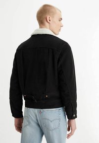 Black denim jacket with a white shearling collar, adjustable back strap, and buttoned cuffs, worn with light blue jeans.