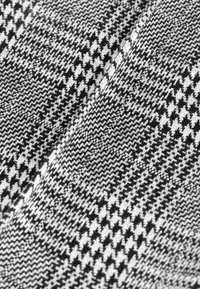 Pletená textilie s proužkovým vzorem houndstooth v černé a bílé barvě. Vyznačuje se hladkým povrchem a střídajícími se diamantovými tvary.