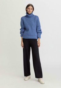 Blauer gestrickter Rollkragenpullover mit gerippter Textur, kombiniert mit schwarzen weit geschnittenen Hosen und weißen Sneakern.