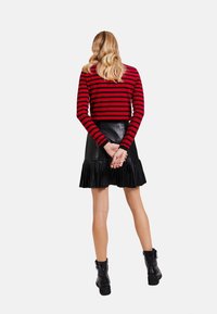 Rotes und schwarzes gestreiftes Langarmoberteil, kombiniert mit einem schwarzen, gefalteten Lederrock. Schwarze Knöchelstiefel runden das Outfit ab.