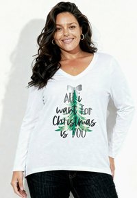 Biała bluzka z długim rękawem i dekoltem w serek, z nadrukiem choinki i napisem, w kolorach zielonym, czarnym i srebrnym. Miękka tkanina, luźny krój.
