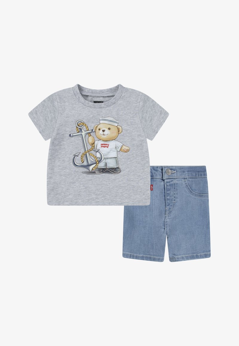 T-shirt grigia a maniche corte con un orsetto dei cartoni animati in abbigliamento da marinaio, abbinata a pantaloni corti in denim blu. La T-shirt ha un collo rotondo e una stampa decorativa.
