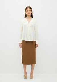 Camicia bianca con colletto a V e maniche lunghe, abbinata a una gonna marrone lunga fino al ginocchio con uno spacco laterale. Scarpe beige semplici.