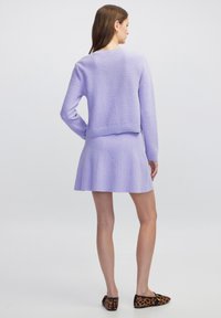 Hellblauer gestrickter Pullover und ausgestellte Mini-Rock mit strukturierter Oberfläche. Kombiniert mit Ballerinas im Leopardenmuster. Sicht von hinten.