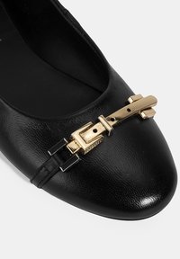 Schwarze Ballerinas aus Leder mit einer spitzen Zehenpartie, ausgestattet mit einer goldenen Schnallenakzentuierung und silbernen Hardware-Details. Glatte Textur, minimalistisches Design.