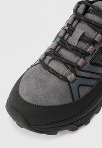 Nahaufnahme der Zehenpartie eines grau-schwarzen Wanderschuhs mit strukturiertem Profil, Obermaterial aus Wildleder und schwarzen Schnürsenkeln, die durch graue Schlaufen gefädelt sind.