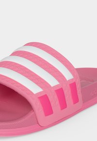 Pinkfarbene Slide-Sandale mit drei erhabenen weißen Streifen auf dem breiten Riemen und einer strukturierten Innensohle für Halt und Komfort.
