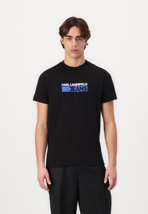 Juodas medvilnės marškinėliai su baltu ir mėlynu "KARL LAGERFELD JEANS" logotipu priekyje. Klasikinis apvalus kaklas ir trumpomis rankovėmis.