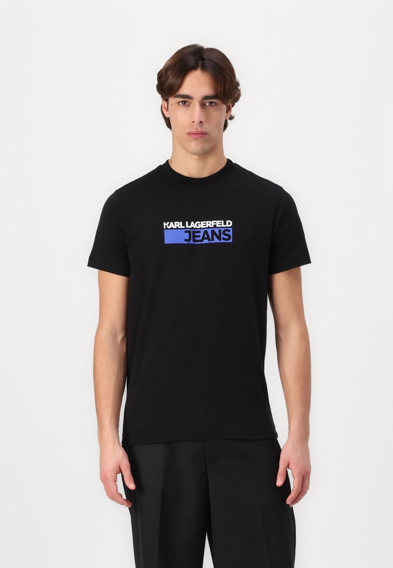 Juodas medvilnės marškinėliai su baltu ir mėlynu "KARL LAGERFELD JEANS" logotipu priekyje. Klasikinis apvalus kaklas ir trumpomis rankovėmis.