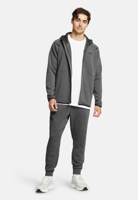 Gray zip-up hoodie with pocket accents, paired with matching pants. White t-shirt underneath and gray sneakers complete the athletic look.