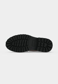 Semelle d'une botte noire avec un motif profond conçu pour l'adhérence et la durabilité sur diverses surfaces.