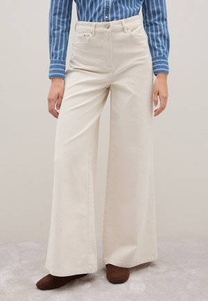 Wijduitlopende, beige broek gemaakt van textuurstof; hoog in de taille met zijzakken, gecombineerd met een blauwe gestreepte shirt.