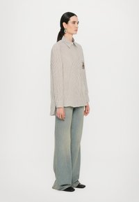 Striped shirt with a tailored collar and an embroidered design, paired with wide-leg denim pants in a light wash. Black flat shoes.