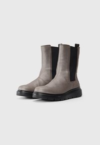 Pareja de botas gris de media pantorrilla con paneles laterales elásticos negros y suelas de goma negra gruesas sobre un fondo claro.