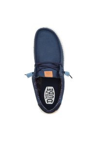 Chaussure slip-on en toile marine avec une semelle en caoutchouc blanche mouchetée, présentant un accent bleu clair près des lacets et une doublure intérieure rayée.