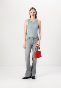 Body blu chiaro a coste, jeans grigi a vita alta con gamba svasata, stivaletti neri alla caviglia e una piccola borsa rossa dal design strutturato.