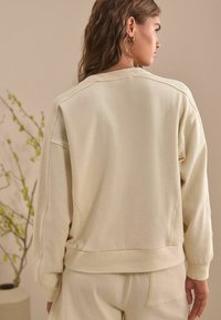 Krämfärgad sweatshirt med texturerad design, oversized passform, ribbade ärmslut och nederkant. Har rund hals och sidopanelsdetaljer.
