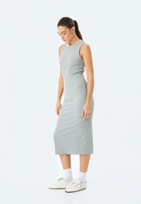 Grijze mouwloze midi-jurk van ribstof met een aangesloten silhouet, gecombineerd met witte sneakers en enkelsokken.