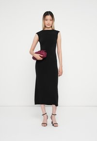Crna, uska midi haljina s kap sleeves i ravnom siluetom. Uparena s maroon clutch-om i crnim sandalama s trakama. Jednostavan dizajn.