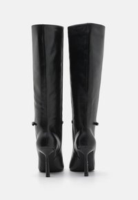 Bottes en cuir noires à hauteur de genou avec un design épuré, bout pointu et talon aigu. Présentent une texture lisse et un minimum de détails.