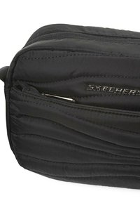 Bolso negro acolchado con una textura suave, que presenta un bolsillo con cremallera y un logo metálico de "SKECHERS". Diseño compacto y aerodinámico.
