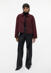 Bordeaux uldjakke med en boxy design, fem sorte knapper og krave. Kombineret med sorte læderbukser med vide ben. Glat tekstur.