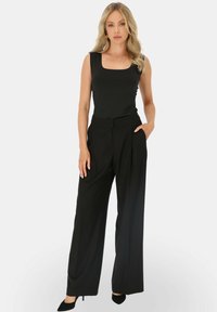 Czarny bezrękawnik z kwadratowym dekoltem zestawiony z czarnymi spodniami o wysokim stanie i szerokich nogawkach; gładka faktura; noszony z czarnymi szpilkami.