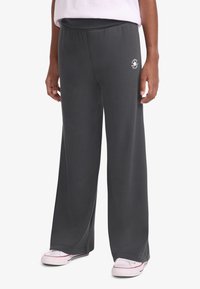 Γκρι φαρδιά φόρμα με απαλό ύφασμα, ελαστική μέση και μικρή λογότυπο στο αριστερό μηρό. Φορώντας με λευκά παπούτσια.