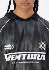 Tricou polo cu dungi negre și gri, având un guler negru. Prezintă logo-urile „VENTURA” și „CORE” în alb. Materialul pare ușor și texturat.