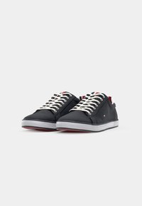 Zwarte canvas sneakers met witte veters, een rubberen zool, rode accenten en een klein merklogo aan de zijkant. Laag profiel ontwerp.