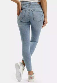 Jasnoniebieskie rurki z wysokim stanem, z dwoma tylnymi kieszeniami i gładką teksturą denimu. Połączone z białymi sneakersami.