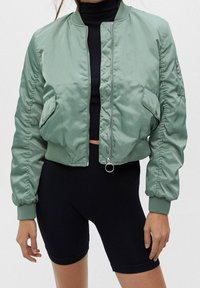 Lichtgroene bomberjack van gladde stof, voorzien van een voorrits, geribbelde manchetten en zijzakken met geplooide mouwen.