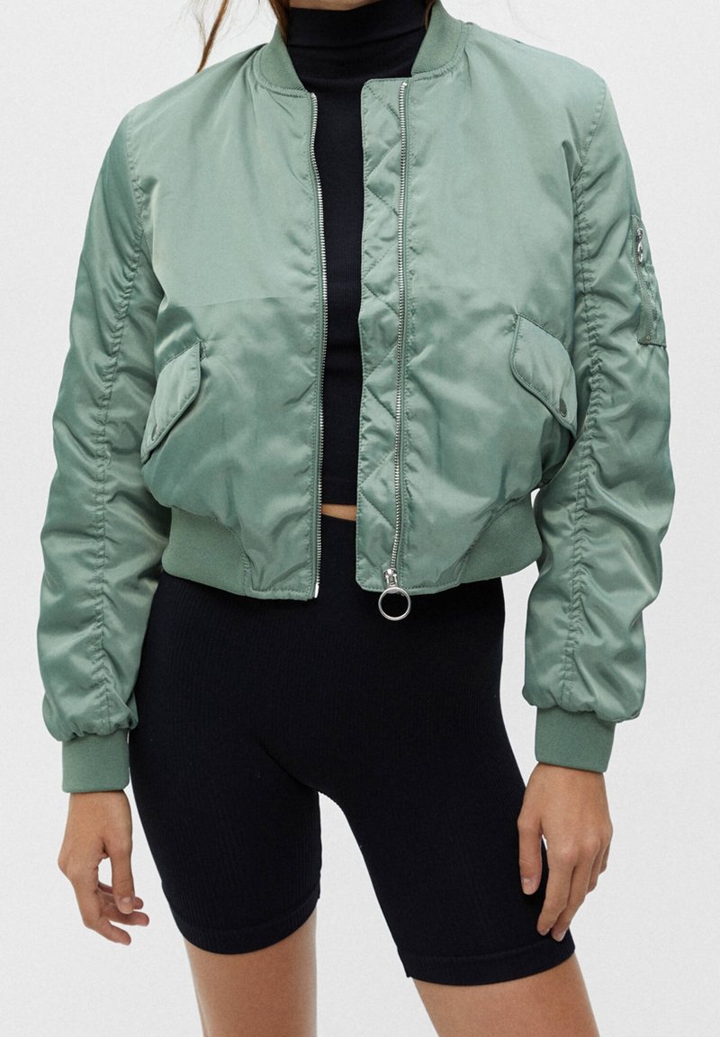 Lichtgroene bomberjack van gladde stof, voorzien van een voorrits, geribbelde manchetten en zijzakken met geplooide mouwen.