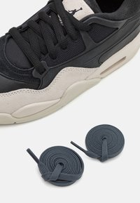 Zapatilla de cuero negro y malla con acentos de gamuza beige, que presenta cordones oscuros redondos y una unidad de aire visible en la suela.