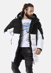 Schwarze und weiße Daunenjacke mit hohem Kragen, Reißverschluss vorne und gestepptem Muster; das Innere hat ein gemustertes Futter.