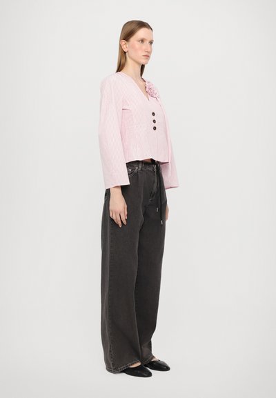 Camicia cropped a righe rosa con scollatura a V e tre bottoni marroni, abbinata a jeans grigi scuri dal taglio morbido e scarpe nere.