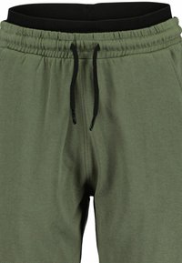 Pantalons de survêtement vert olive en tissu doux avec une taille élastique noire et un cordon de serrage noir, dotés de coutures latérales pour un fit décontracté.