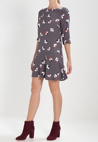 Robe grise à manches trois-quarts, ornée d'un motif floral en rose, rouge et bleu marine. Associée à des bottines bordeaux.