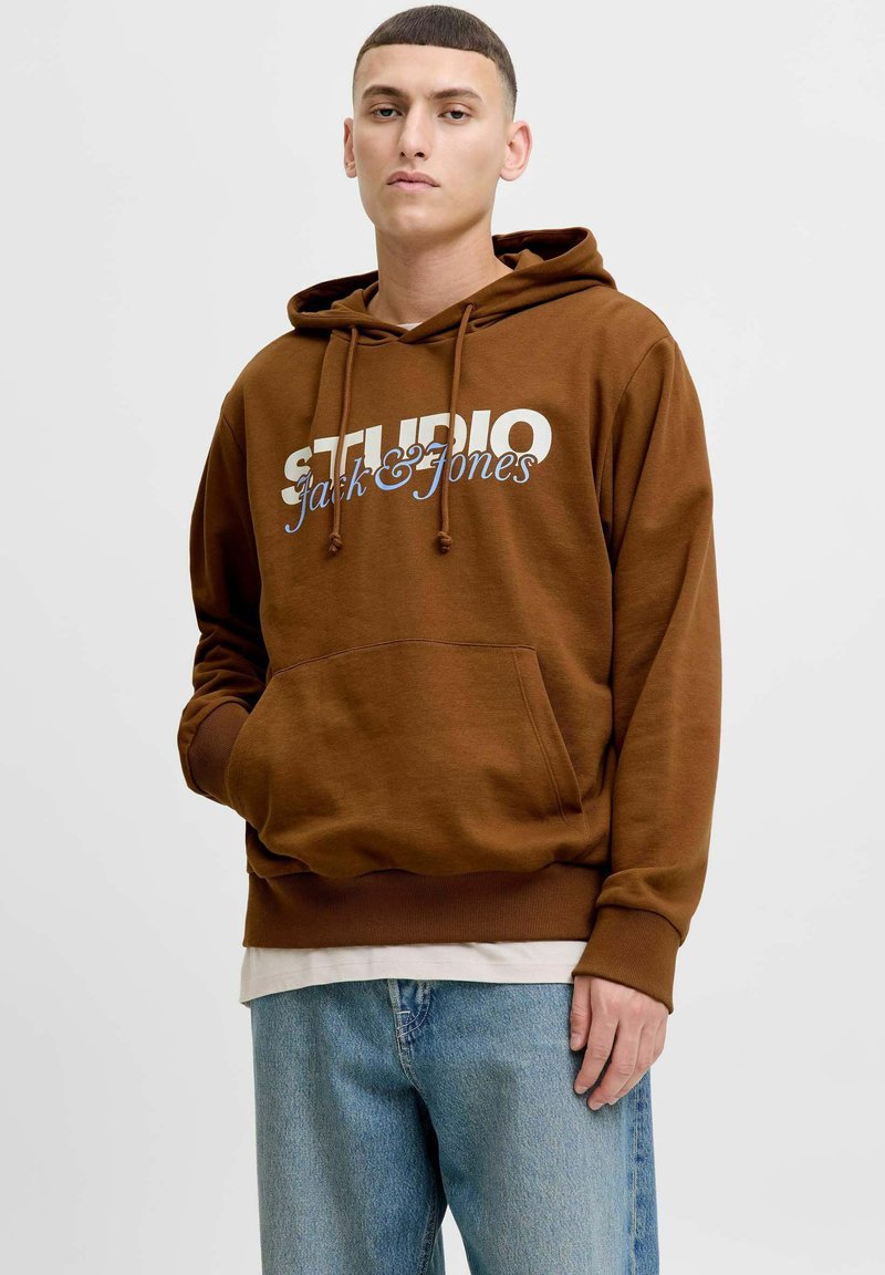 Hnědá mikina s kapucí a přední kapsou, se stahovací šňůrkou a bílým logem "STUDIO Jack & Jones". Obsahuje žebrované manžety a lem, z materiálu ze směsi bavlny.