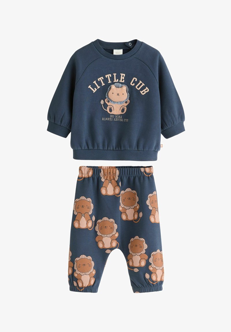 Temno modra dukserica z grafiko leva in besedilom, v kombinaciji z ustreznimi hlačami z ponavljajočim se vzorcem leva. Narejena iz mehkega, udobnega materiala.