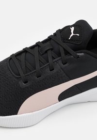 Černá sportovní bota s texturovaným textilním svrškem, která má světle růžový akcentový pruh a bílou podešev. Krajkový design s logem na jazyku.