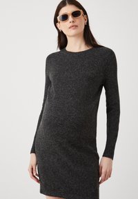 Szürke kötött ruha hosszú ujjakkal, kerek nyakkivágással és testhez simuló vonalakkal. Simma textúra finom színeltérésekkel.