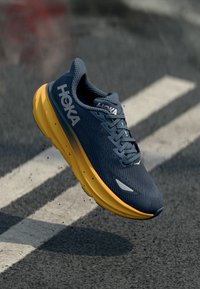 HOKA running shoe with a textured dark blue upper, yellow midsole, and grey accents. Features traditional lacing and lightweight design.
