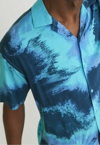 Hombre con una camisa de botones de manga corta con un patrón abstracto en acuarela de color azul y turquesa.